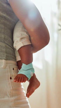 A parent holding a baby, with an Owlet sock on the baby's foot