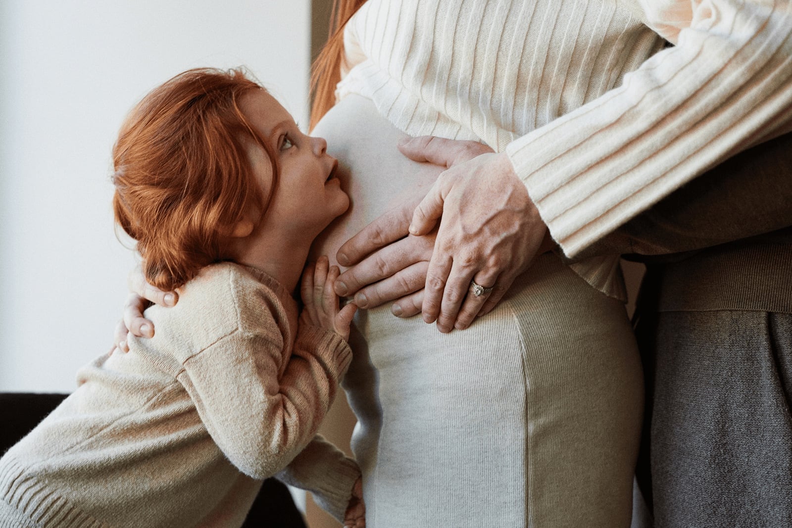 An expecting parent with their toddler leaning in to listen to the bump
